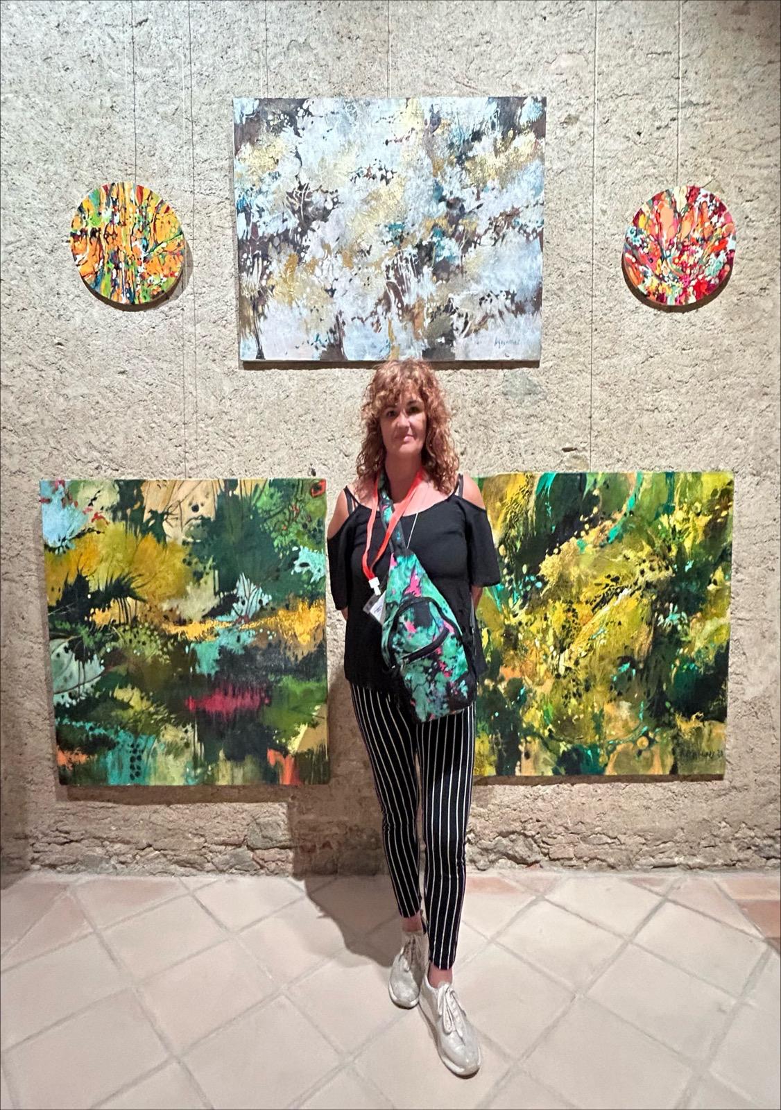 Artista junto a varias obras abstractas expuestas